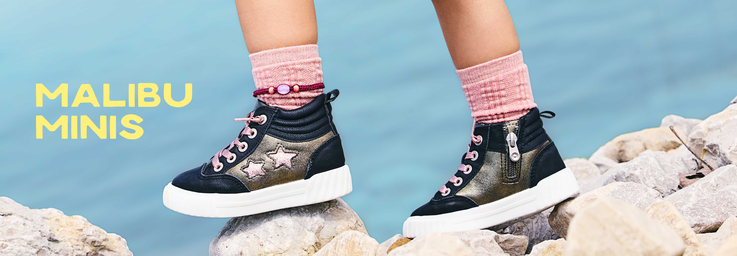 Child’s legs wearing black and gold high-top sneakers with pink stars and pink socks, standing on rocks.