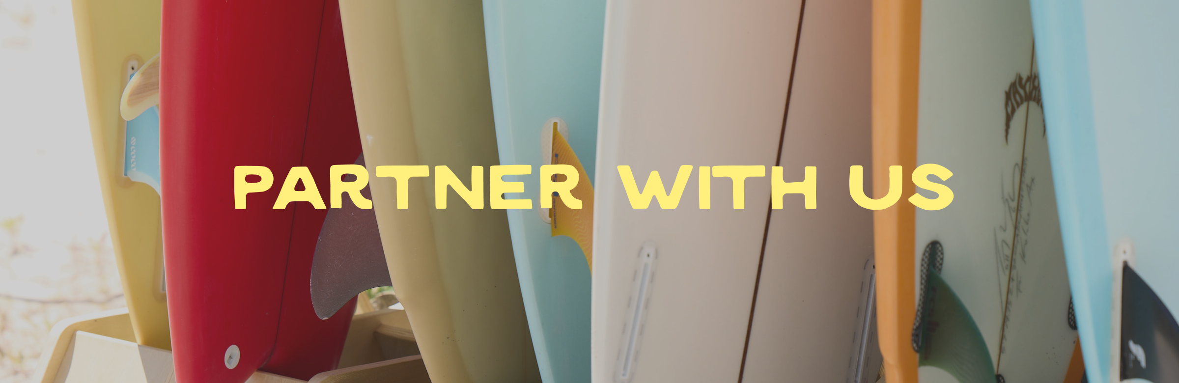 Close-up of surfboards in various colors standing upright with 'Partner With Us' text overlay.